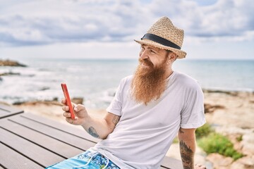 Sticker - Young redhead tourist man using smartphone sitting on the bench at the beach.