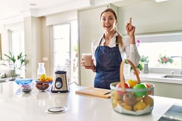 Poster - Beautiful blonde woman wearing apron drinking smoothie at the kitchen surprised with an idea or question pointing finger with happy face, number one