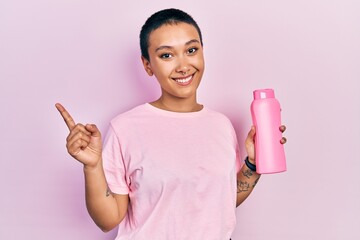 Sticker - Beautiful hispanic woman with short hair holding shampoo bottle smiling happy pointing with hand and finger to the side