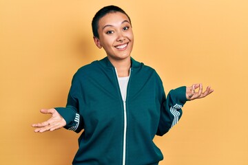 Poster - Beautiful hispanic woman with short hair wearing sporty jacket clueless and confused expression with arms and hands raised. doubt concept.