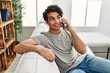 © Krakenimages.com - Young hispanic man talking on the smartphone sitting on the sofa at home.