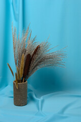 Autumn bouquet of cattails and reeds on a textured background made of soft blue fabric with elegant pleats.