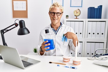 Poster - Young blond dentist man holding mouthwash at clinic pointing finger to one self smiling happy and proud