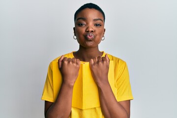 Sticker - Young african american woman holding book puffing cheeks with funny face. mouth inflated with air, catching air.