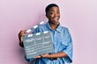 © Krakenimages.com - Young african american woman holding video film clapboard winking looking at the camera with sexy expression, cheerful and happy face.