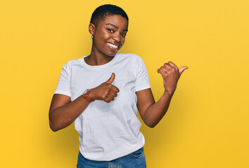 Young african american woman wearing casual white t shirt pointing to the back behind with hand and thumbs up, smiling confident