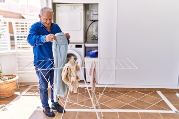 Wall Mural - Senior caucasian man smiling happy putting clothes on clothesline at the terrace.