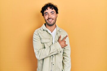 Sticker - Young hispanic man wearing casual clothes cheerful with a smile of face pointing with hand and finger up to the side with happy and natural expression on face