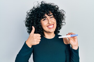 Sticker - Young middle east woman holding pregnancy test result smiling happy and positive, thumb up doing excellent and approval sign