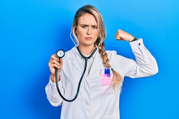 Sticker - Beautiful young blonde doctor woman holding stethoscope strong person showing arm muscle, confident and proud of power