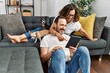 © Krakenimages.com - Middle age hispanic couple smiling happy and using touchpad. Sitting on the sofa with dogs at home.