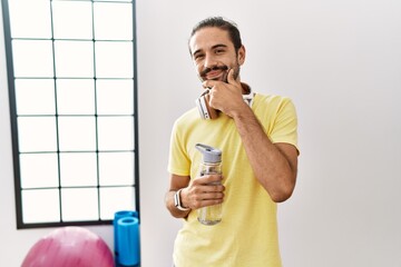 Sticker - Young hispanic man wearing sportswear and drinking water at the gym looking confident at the camera smiling with crossed arms and hand raised on chin. thinking positive.