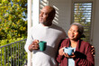 Relaxed african american senior couple drinking coffee standing on balcony in sun