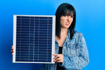 Sticker - Young hispanic woman holding photovoltaic solar panel clueless and confused expression. doubt concept.