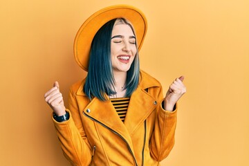 Sticker - Young modern girl wearing yellow hat and leather jacket very happy and excited doing winner gesture with arms raised, smiling and screaming for success. celebration concept.