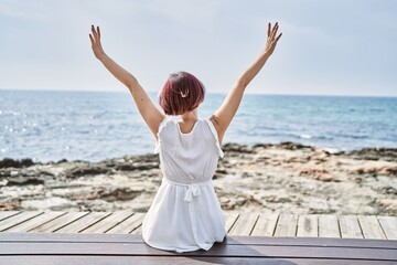 Poster - Young caucasian girl on back view sitting on the bench with hands raised up at the beach.