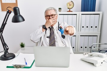 Sticker - Senior caucasian man wearing doctor uniform and stethoscope at the clinic laughing at you, pointing finger to the camera with hand over mouth, shame expression