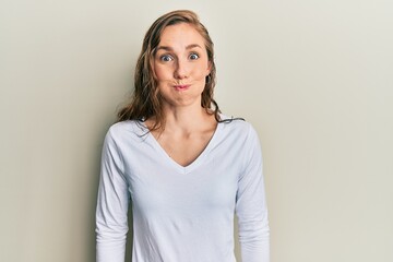 Wall Mural - Young blonde woman wearing casual clothes puffing cheeks with funny face. mouth inflated with air, crazy expression.