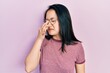 Young chinese girl wearing casual clothes and glasses smelling something stinky and disgusting, intolerable smell, holding breath with fingers on nose. bad smell