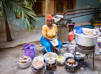 Wall Mural - African woman cooking traditional food at street