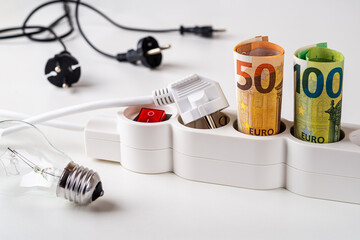 Fifty and one hundred euro banknotes plugged into the extension socket, few electric plugs and light bulb over desk. Increasing of electricity cost, expensive energy, rise in electricity prices. 