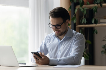 Poster - Smiling businessman in glasses using smartphone at workplace, successful confident man entrepreneur freelancer sitting at home office desk, typing writing message in social network, browsing apps