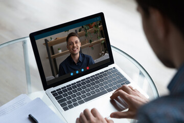 Wall Mural - view over businessman freelancer shoulder chatting online by video call, smiling colleague or mentor