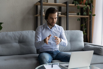 Wall Mural - confident man in wireless headset talking, consulting client, working online at home, serious busine