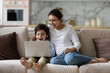 © fizkes - Joyful young indian woman cuddling laughing small cute kid son, watching together funny comedian movie or cartoons online on laptop, relaxing on couch, tech addiction concept.