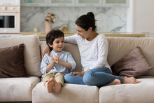 Caring Young Indian Mother Involved In Sincere Conversation With Adorable Small Child Son, Communicating Sitting On Comfortable Sofa, Spending Weekend Leisure Time Together At Home.