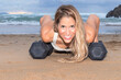 blonde woman doing push-ups on the beach on two dumbbells at sunset