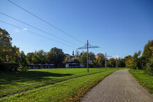 Autumnal Landscape Background With Clear Blue Sky. City Buses In The Parking. Electric Poles For Trams. Green Grass Covered With Dry Golden Leaves. Kopli, Tallinn, Estonia, Europe. September 2021