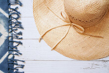 Brown Floppy Straw Hat For Lady With Blue Tie Dye Beach Shawl On White Wooden Background , Summer And Holiday Concept