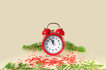 Wall Mural - Evergreen spruce branches, red alarm clock and New Year's confetti on beige paper background.  5 minutes before the New Year.