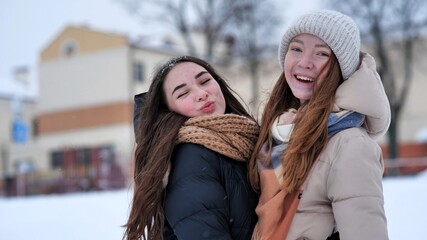 Wall Mural - Portrait of two young smiling and hugging girls in the winter in the city.