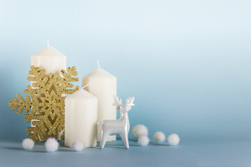 Christmas, New Year composition with three white candles, white porcelain reindeer, golden snowflake and white balls on blue yellow background