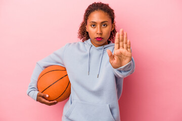 Young african american man playing basketball isolated on pink background standing with outstretched hand showing stop sign, preventing you.