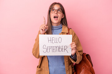 Wall Mural - Young caucasian student woman holding hello September placard isolated on pink background pointing upside with opened mouth.