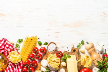 Pasta ingredients on white kitchen table. Raw Pasta, parmesan, olive oil, spices, tomatoes and basil. Top view with copy space.