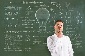 Wall Mural - Attractive thoughtful young european businessman with abstract lamp sketch with mathematical formulas on chalkboard/blackboard wall background. 