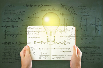 Wall Mural - Hand holding open book with abstract light bulb sketch with mathematical formulas on chalkboard/blackboard wall background. Intelligence, idea, solution, science and innovation concept.