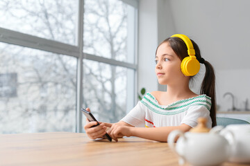 Wall Mural - Little girl with headphones and phone listening to audiobook at home