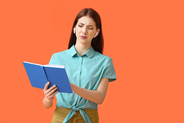 Wall Mural - Displeased young woman with earphones and book on color background