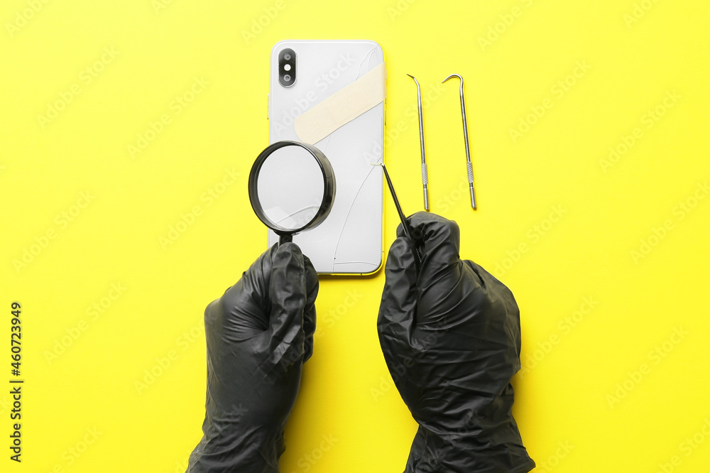 Technician repairing damaged mobile phone on yellow background