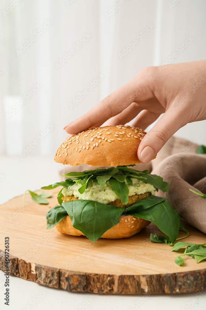 Woman preparing tasty vegetarian burger at table