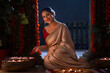 © IndiaPix - Indian gorgeous woman posing in front of camera with flowers in hand while decorating entrance on Diwali