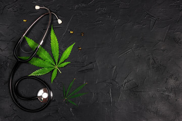 Top view of green cannabis leaves and a stethoscope on black background with copy space.