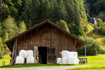 Wall Mural - Farmer barn in Switzerland with the forest and a waterfall in the background