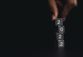 Poster - 2022 Happy New year with the business goal concept. Hand putting a black dice on the top of the 2022 year numbers stack of dice blocks on dark background with copy space, modern and minimal style.