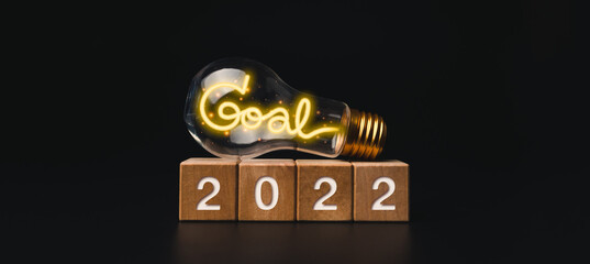 Poster - 2022 Happy New year banner with goal target and successful concept. The 2022 numbers on wooden cube blocks and a light bulb with shining neon light words on dark background, modern and minimal style.